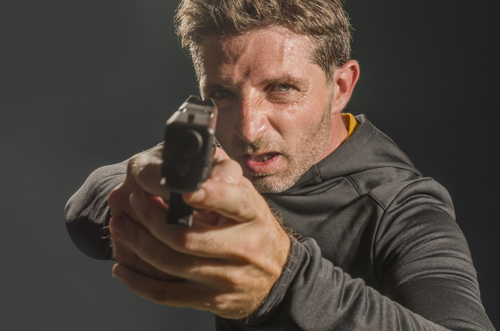 A man holding a gun on a dark background.