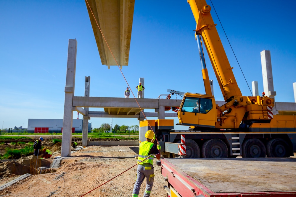 A yellow crane on a construction site with a worker using rigging on the load