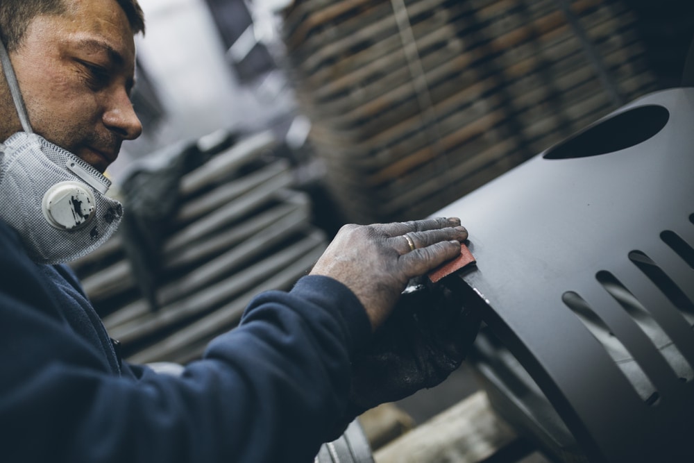 A man wearing a mask is working on a metal object.