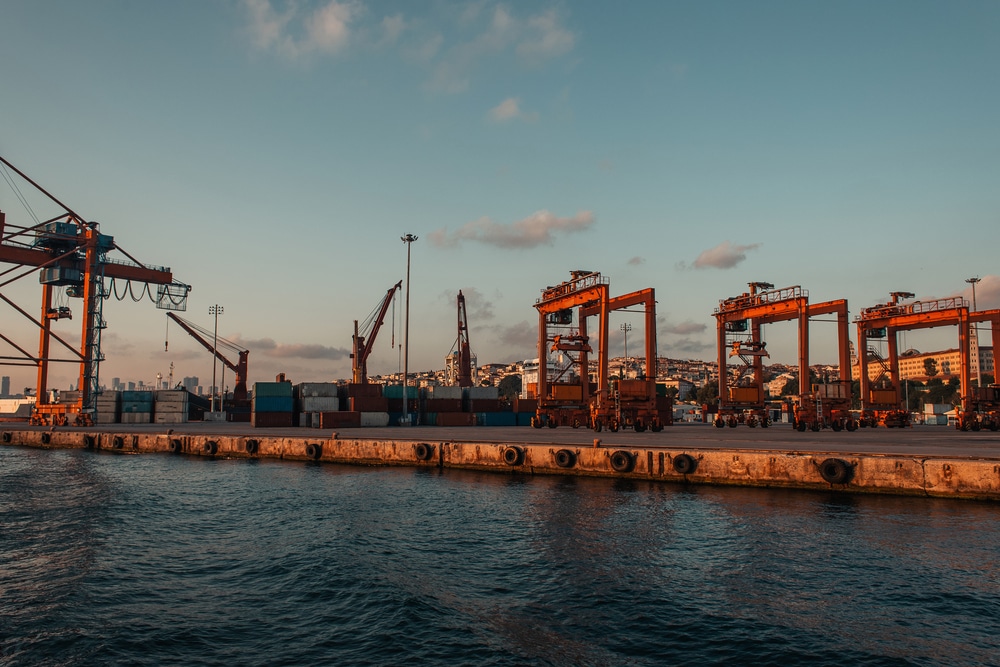 A large container ship docked at a harbor with a row of overhead cranes