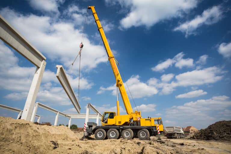 A yellow crane is lifting a piece of concrete.