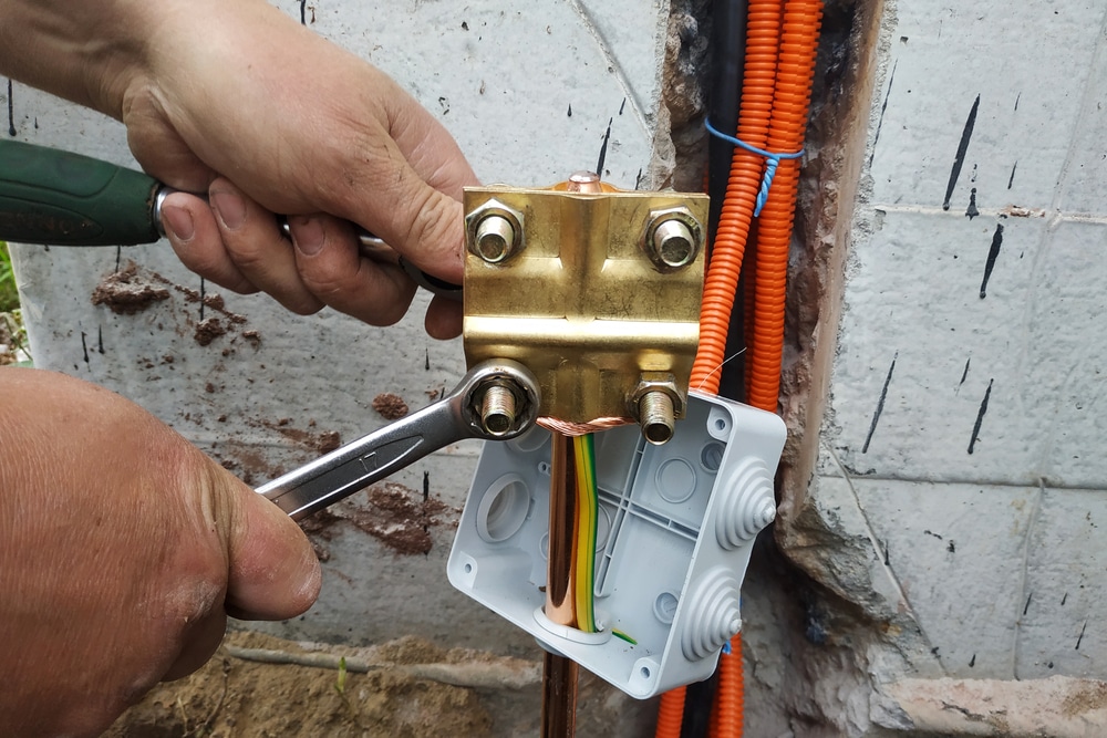 A person is working on an electrical outlet, that has a grounding rod going into the ground.