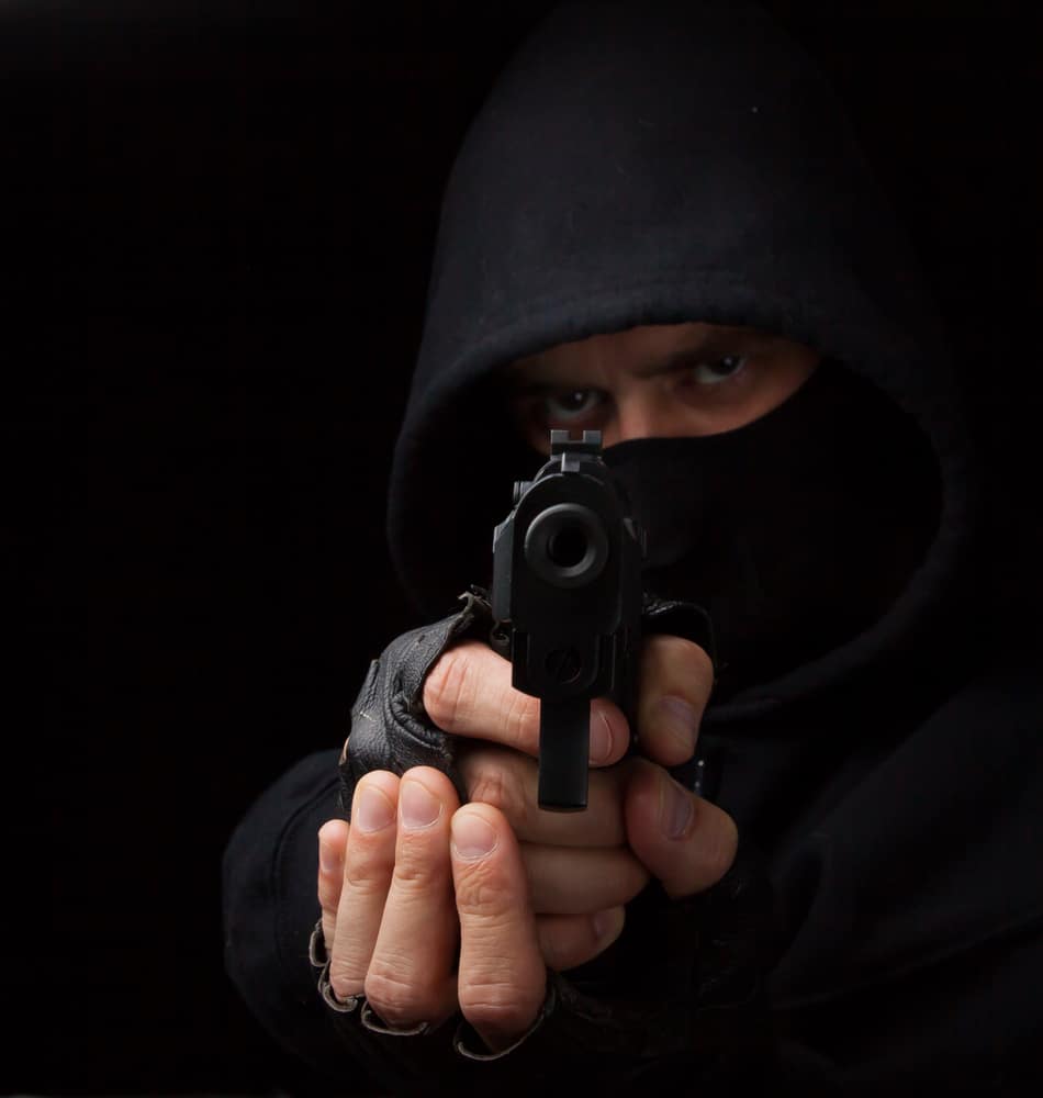 A man in a black hoodie holding a gun.