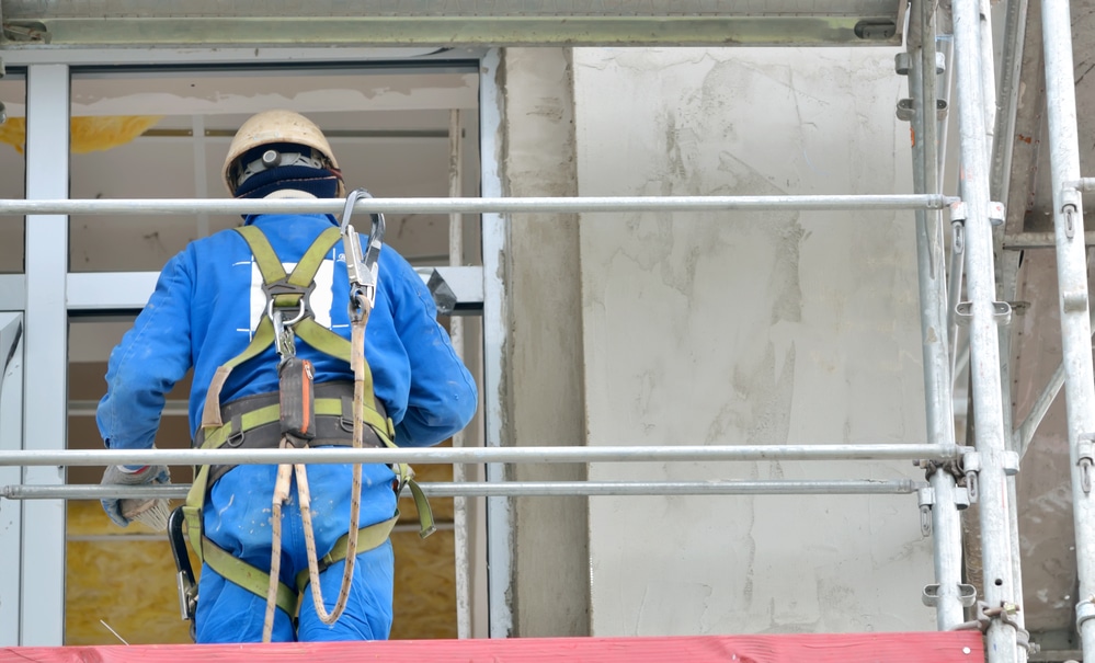 A construction worker is working on a building with scaffolding while wearing a fall protection harness.