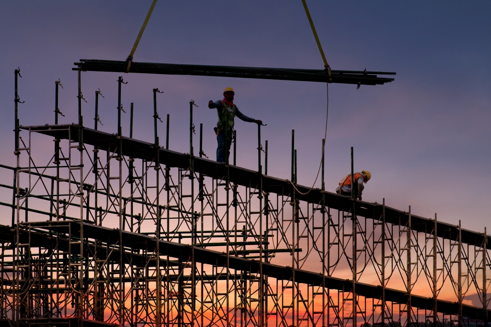 Two construction workers working on a scaffolding at sunset.
