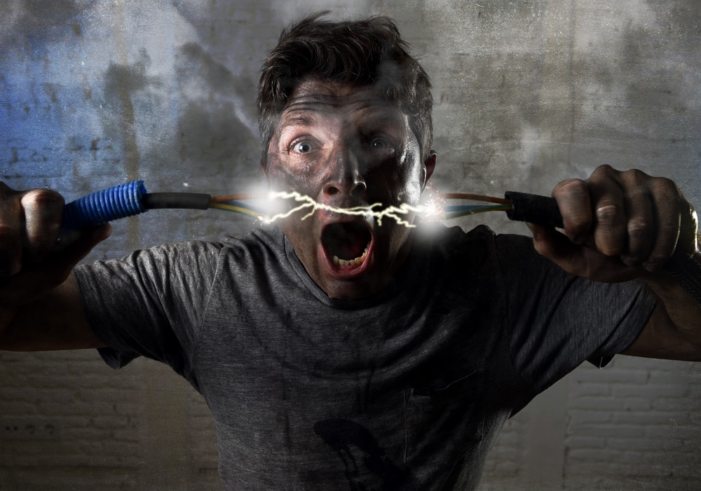 A man holding a wire with his mouth open. He is being electrocuted by the electrical current
